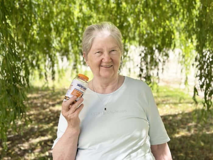 Natural Pharmaceuticals Movisan Eakas naine hoiab käes Moviscal liigeste toetuseks mõeldud toidulisandi pudelit rohelises pargis.